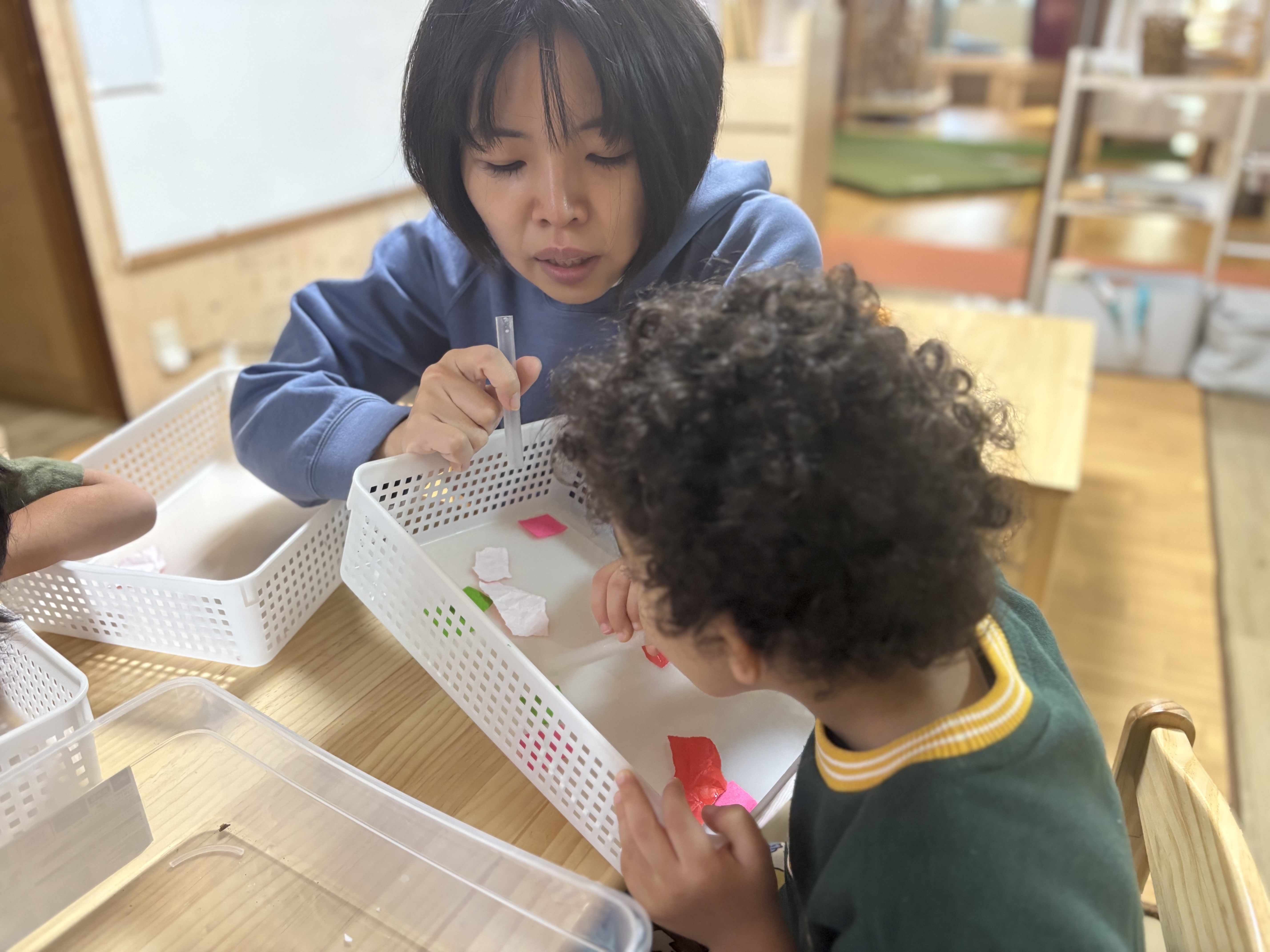 小さな紙をストローで吸って箱へ運ぶゲーム。口の周りの筋肉と呼吸のコントロールを鍛える遊びに必死な先生と子どもたち
