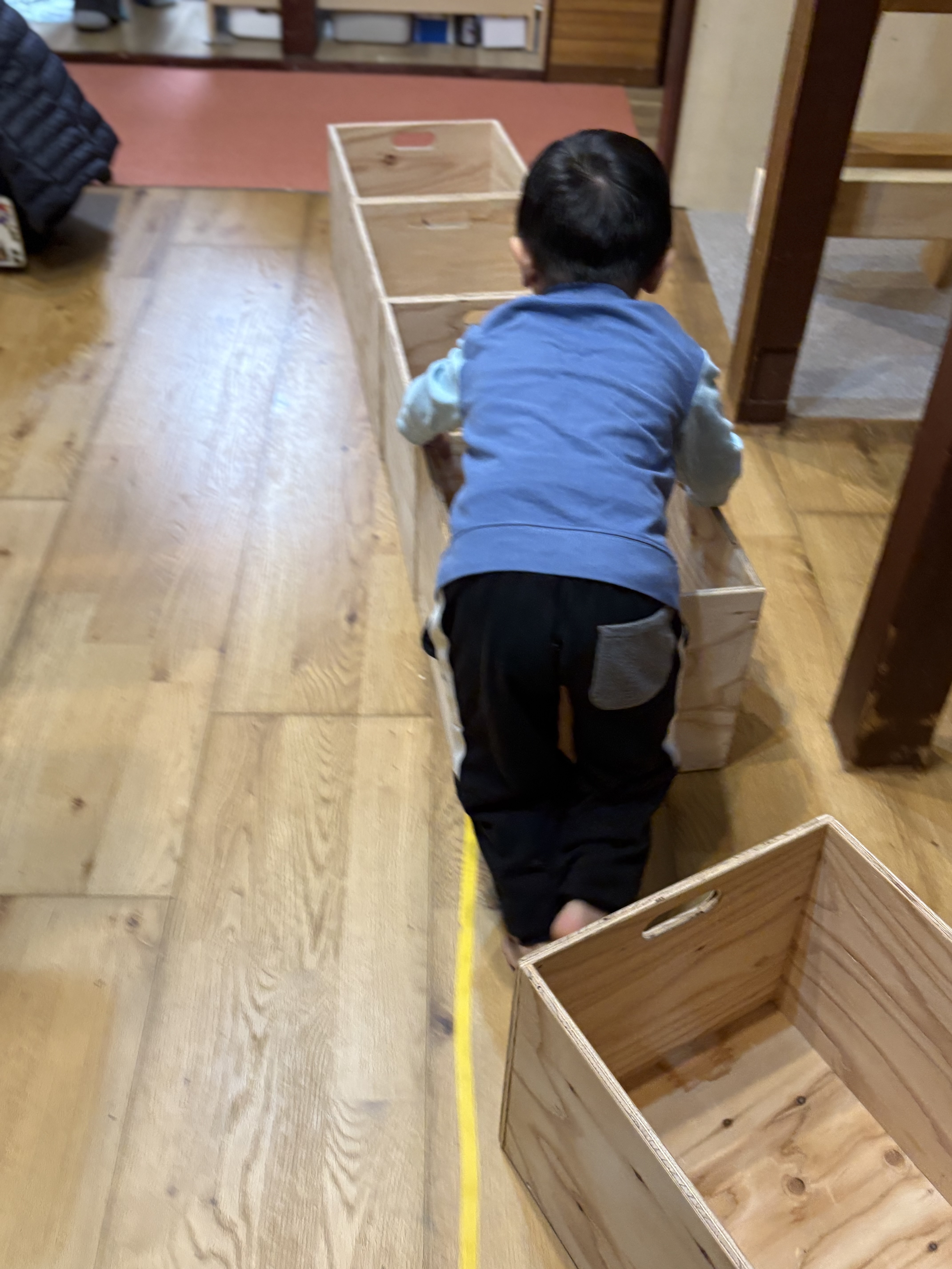 鞄入れのボックスを電車の車両にして電車ごっこする男の子。