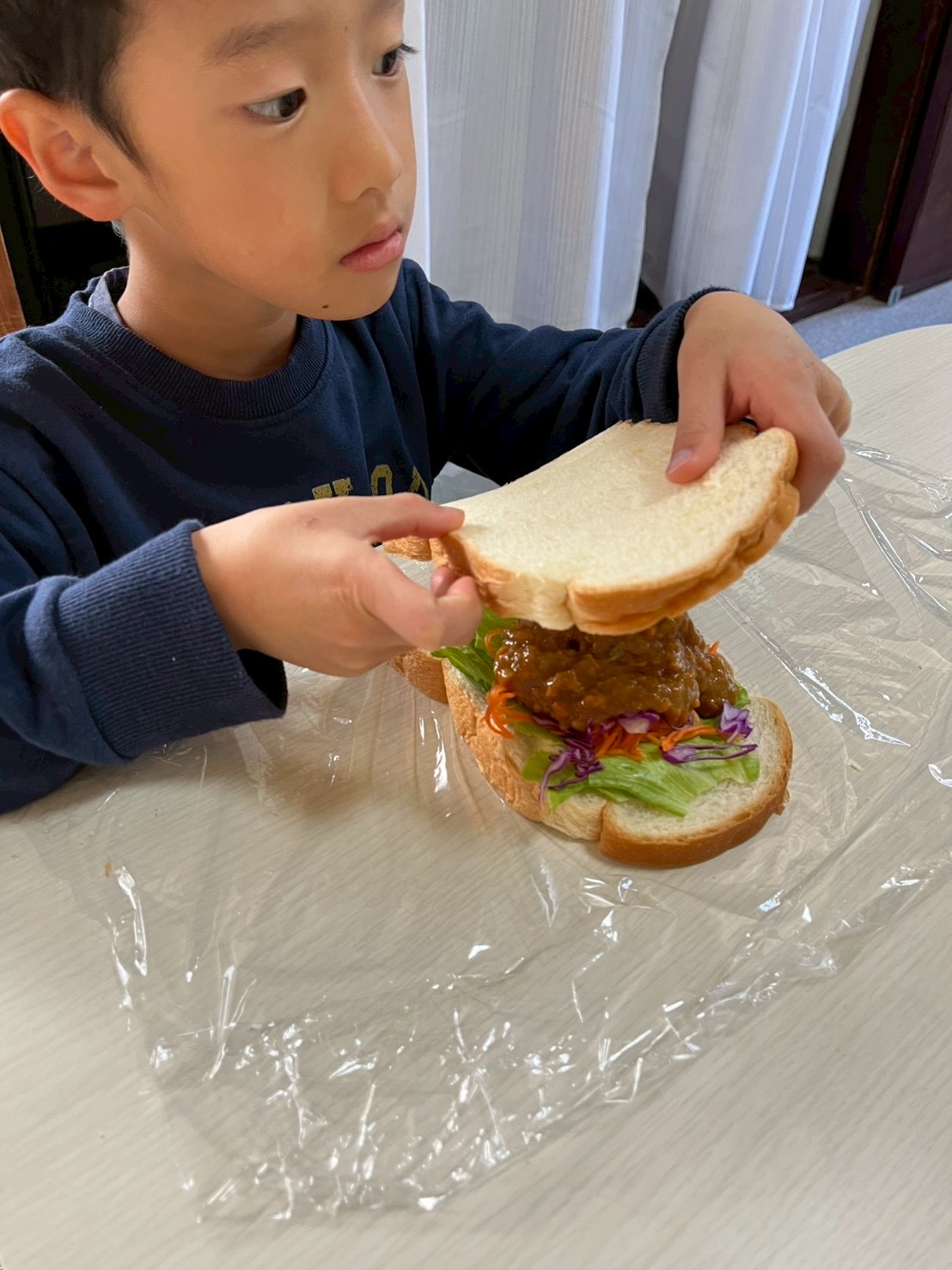 パンをサンドする時の力加減が難しい。両手でパンを持って具材がこぼれないようにコントロールする男の子。