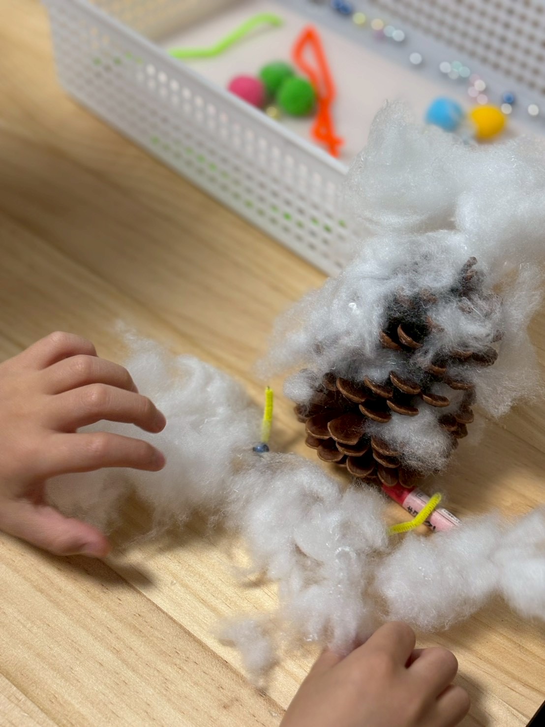 こんなのも付けたら綺麗かな？あれも付けたいなと、目の前にある気になるものを沢山松ぼっくりにくっつける場面。