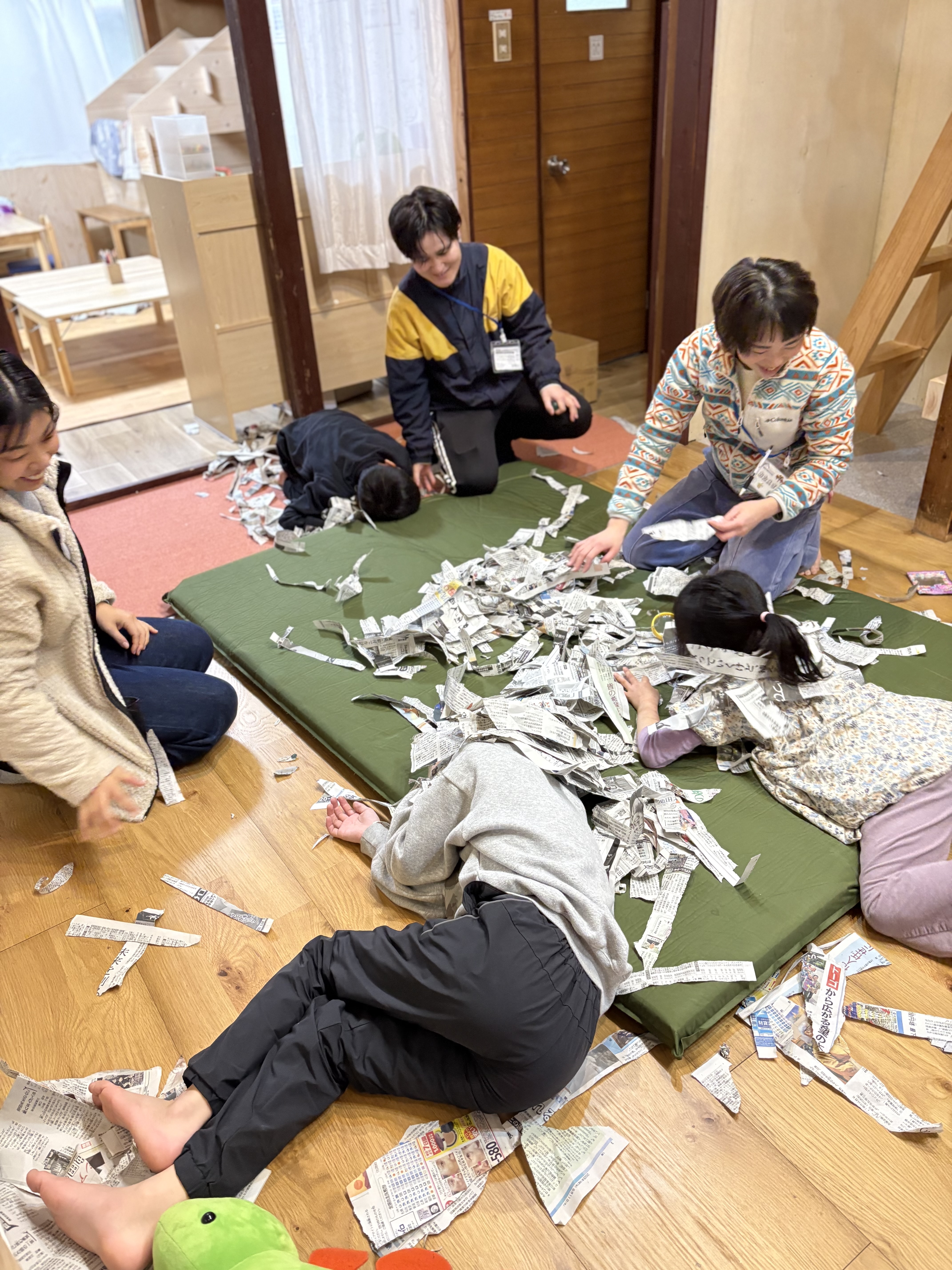 「指先のセンサー発動。」大量の新聞紙の中から、小さなビー玉を真剣な表情で探り当てる手元のアップ。