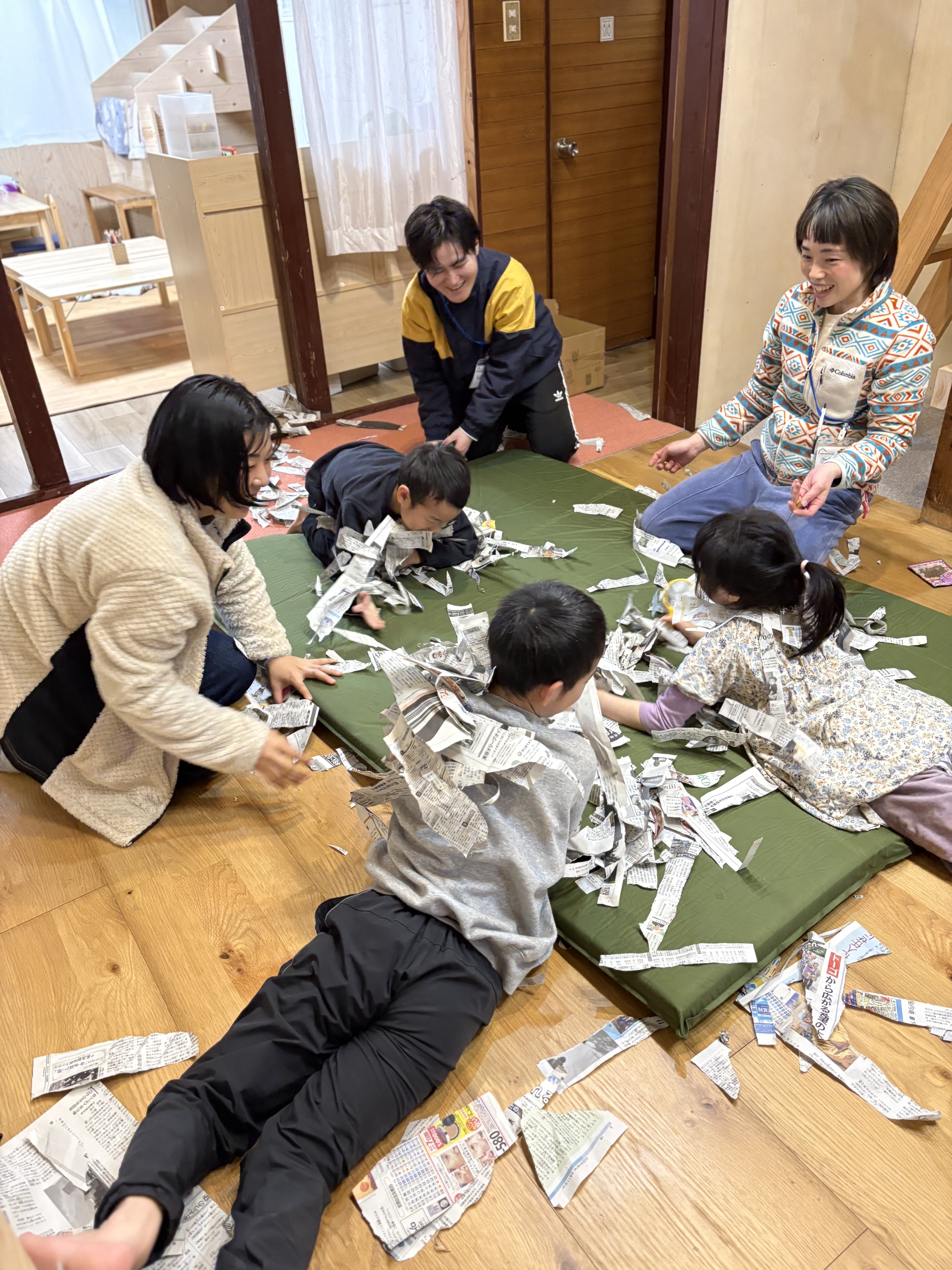 「新聞紙の海へダイブ！」部屋を埋め尽くすカサカサの波に、全身で飛び込む子どもたちの後ろ姿。