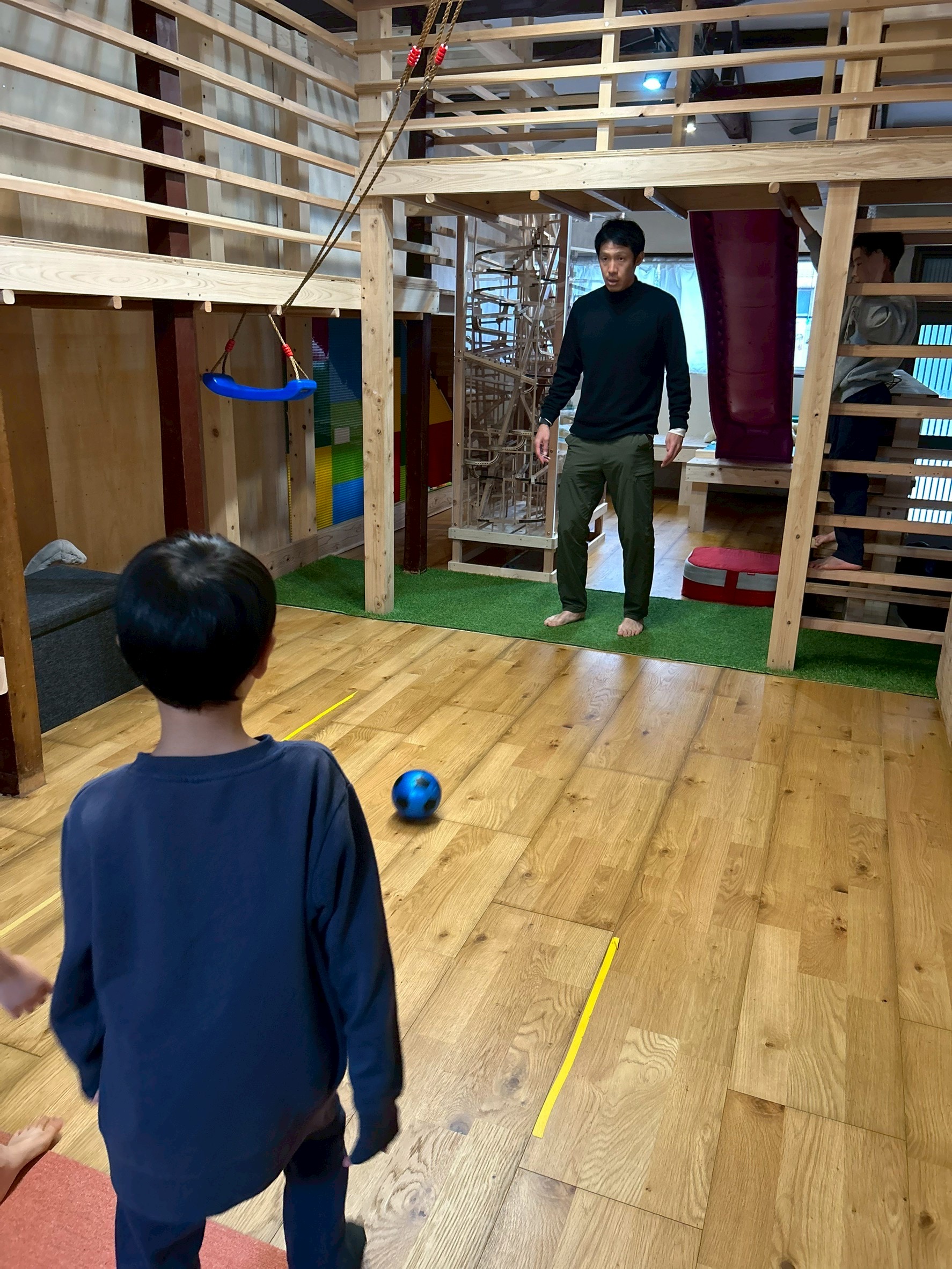 「あの日、僕を救ってくれたボール。」 芝生の上に置かれたサッカーボールと、それを見つめるこばやんさんの後ろ姿。言葉の壁を超えて自分を解放できた、情熱の始まりを感じさせる1枚。