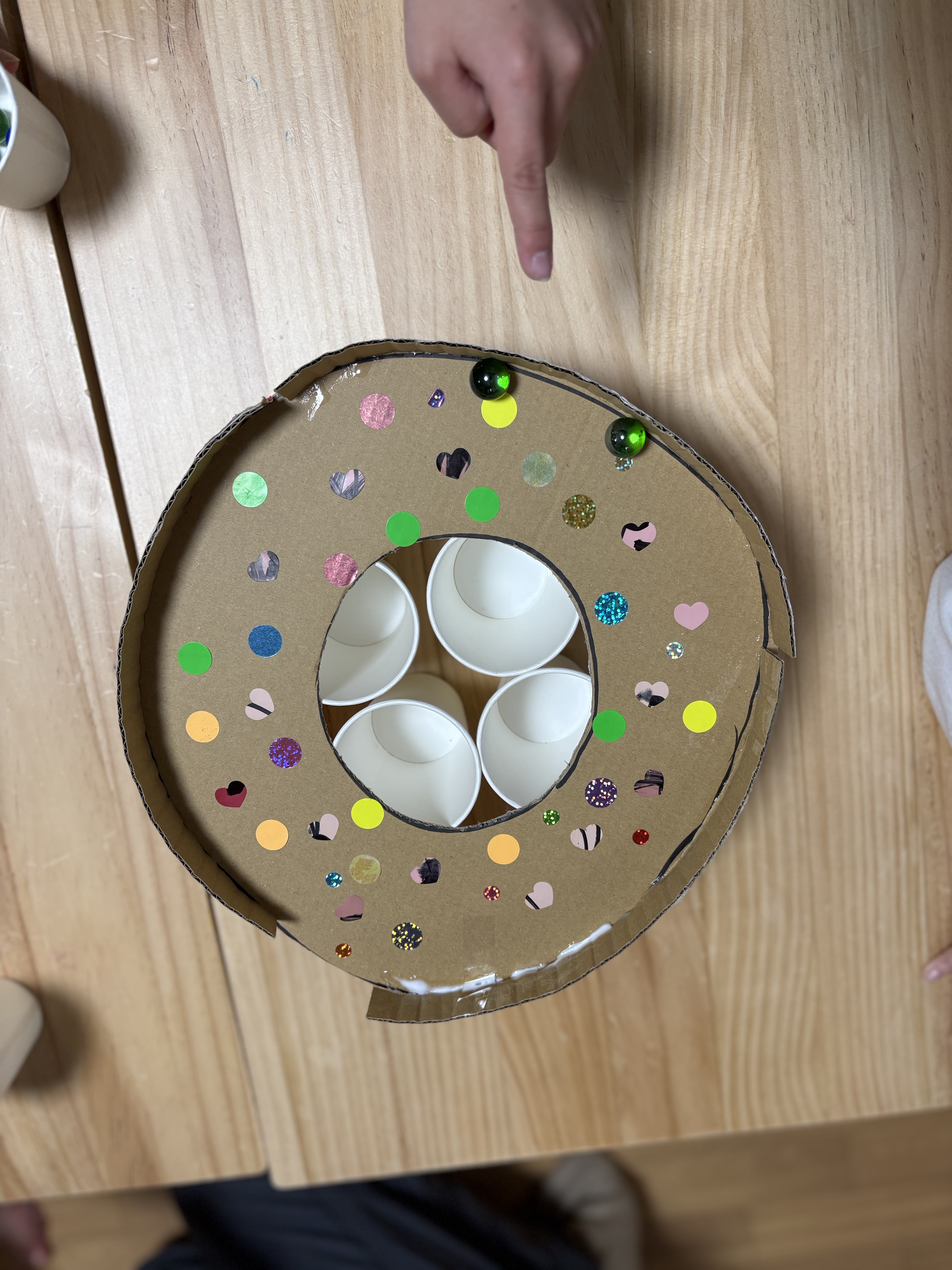 「スタッフの愛が詰まった自信作！」

段ボールと紙コップでできた温かみのある「ビー玉落としマシーン」の全体像。