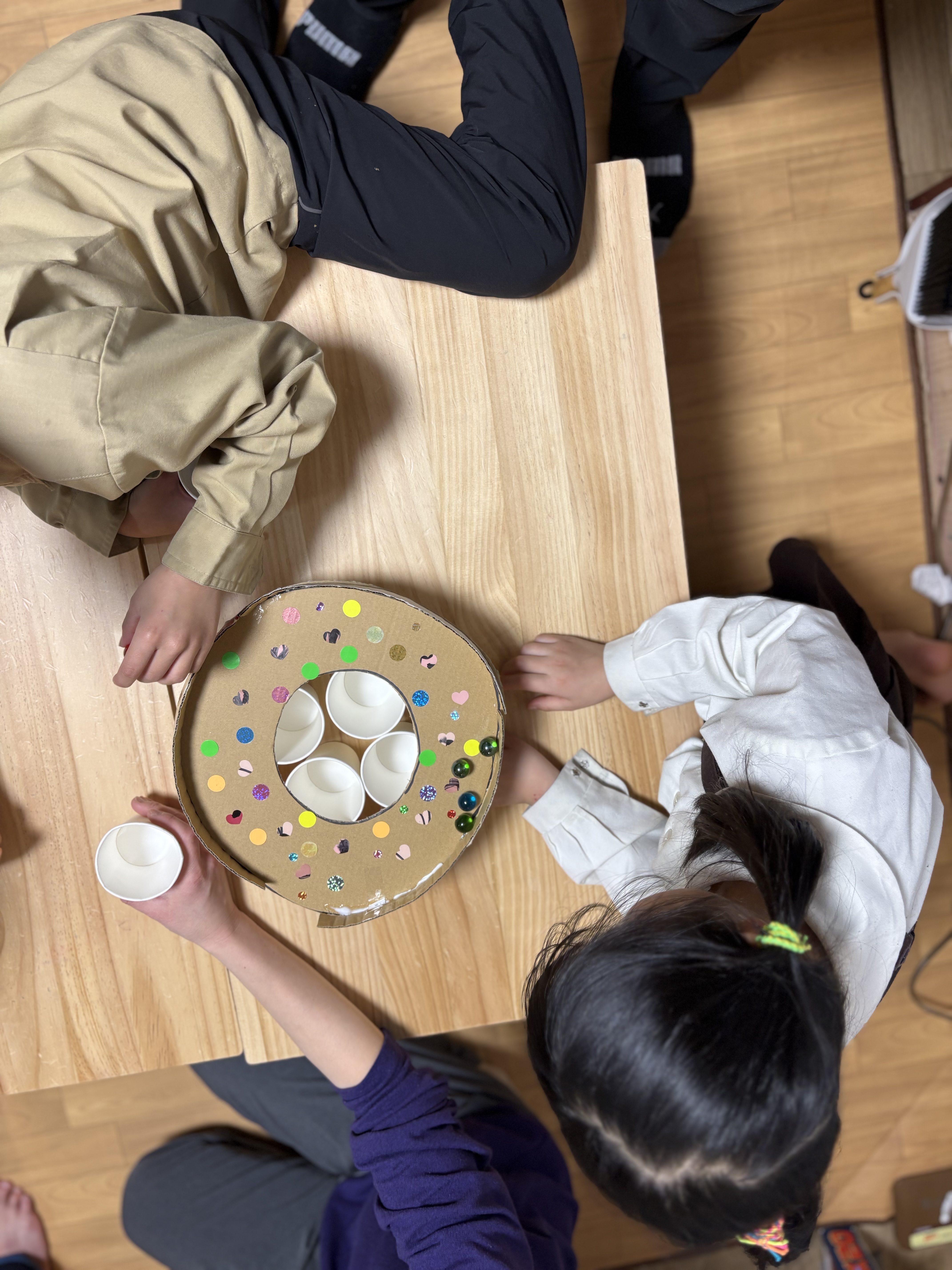 マシーンを囲む、小さな輪。」

順番を待つ子と遊ぶ子が、一つの手作りおもちゃを囲んで穏やかに過ごすハウスの日常。