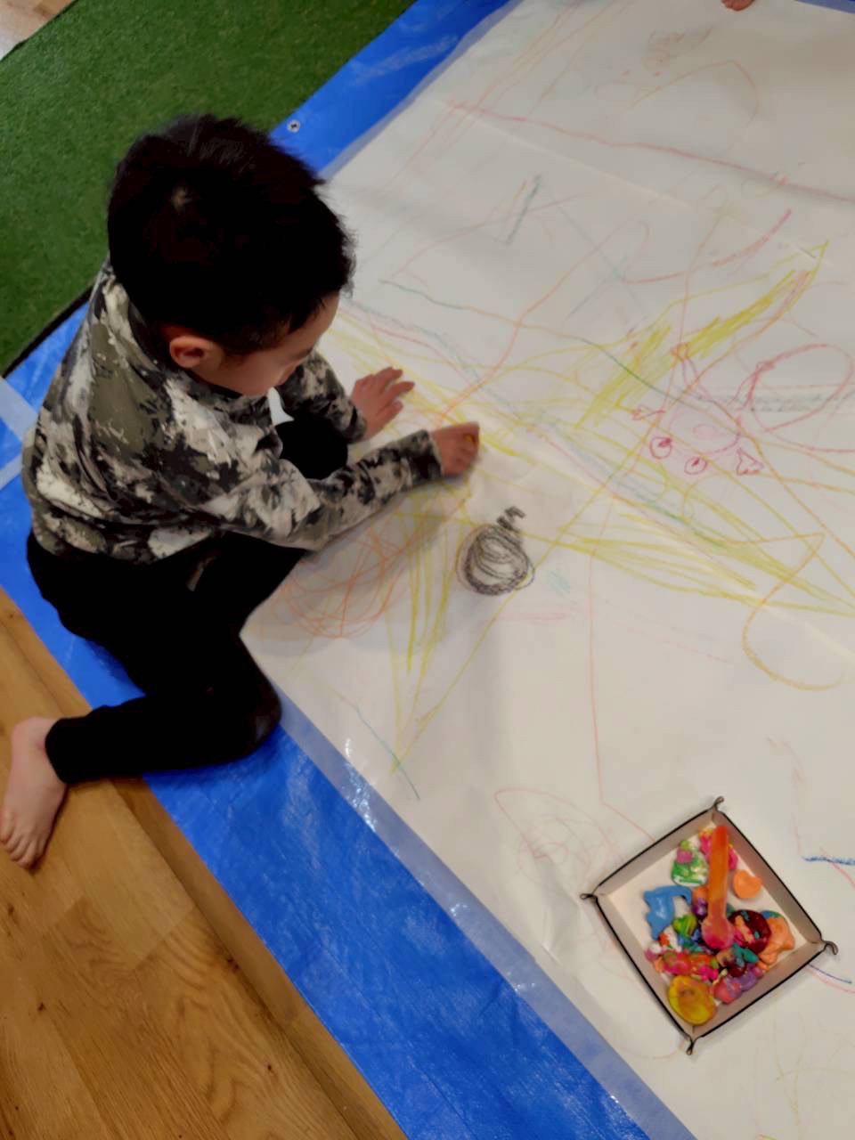 「完成したクレヨンと、誇らしげなドヤ顔。」

自分の作品を胸の前に掲げ、「僕が作ったんだよ！」とカメラ（お母さん）に向かって見せる自信満々の表情。