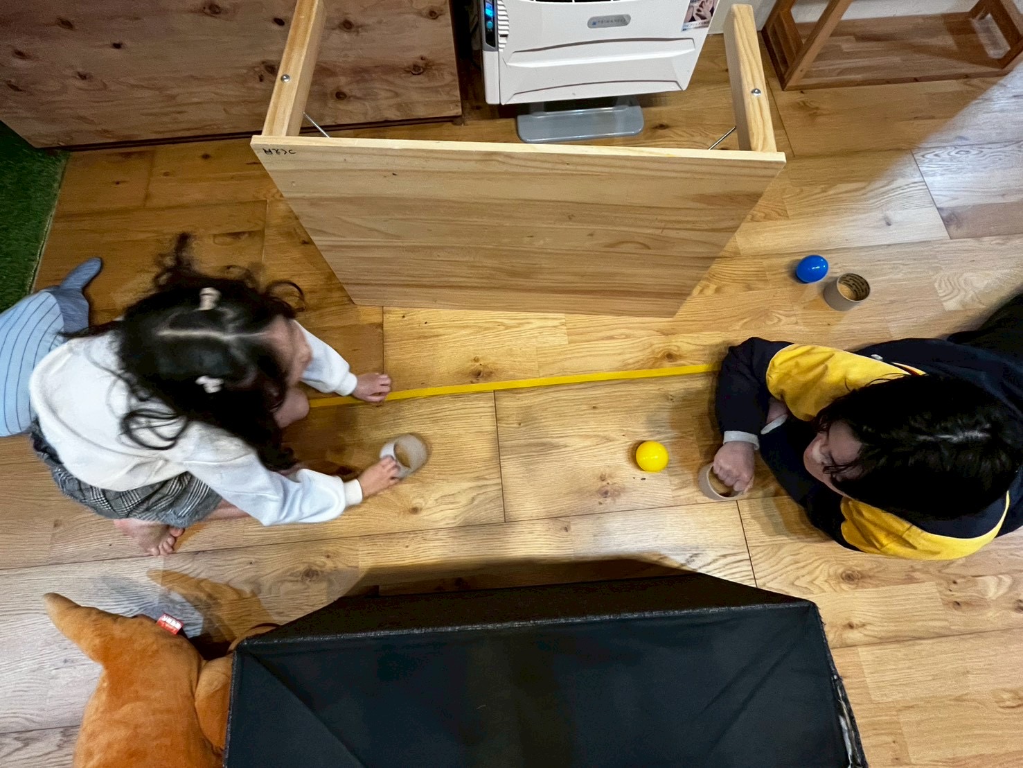 「狙いを定めて、全集中。」

屈み込んで床スレスレの視線でパック（キャップ等）を見つめ、ゴールを狙う瞬間。目の動き（追視）と手の連動が試される、アスリートのような眼差し。