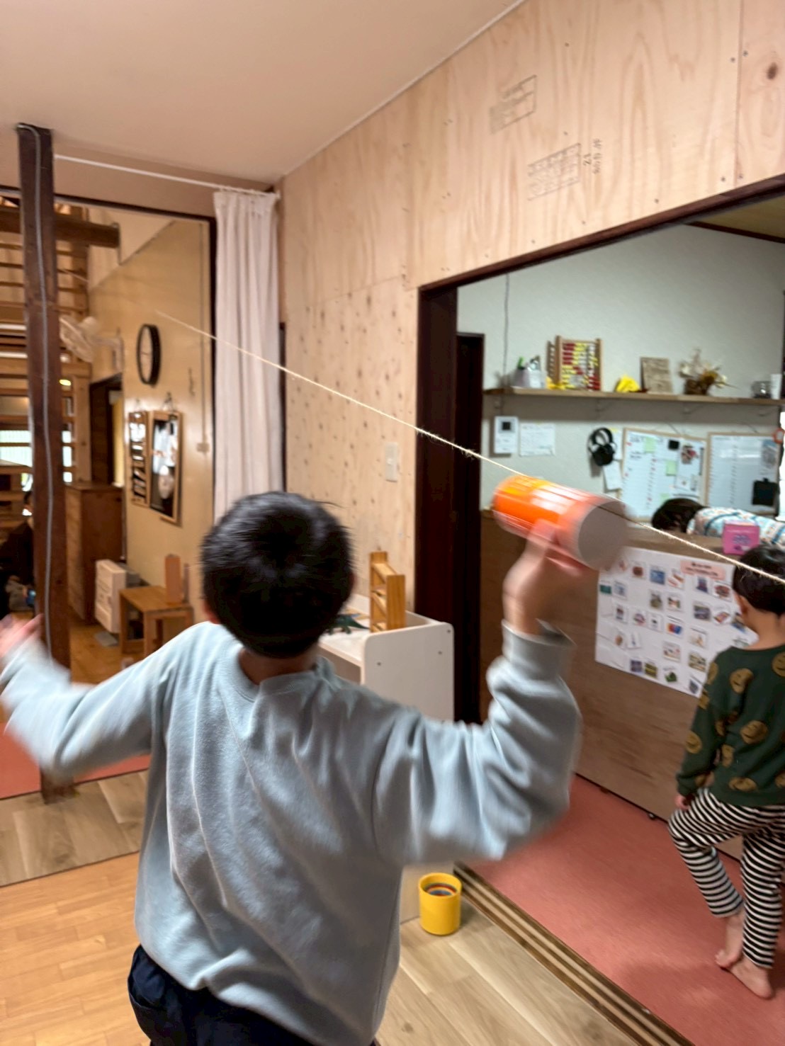 「テイクオフ！空飛ぶポテチ箱。」

手を離した瞬間、箱が紐に沿ってシュッ！と勢いよく斜め上へ駆け上がる躍動感溢れるカット。吹き抜けの開放感が伝わるアングル。