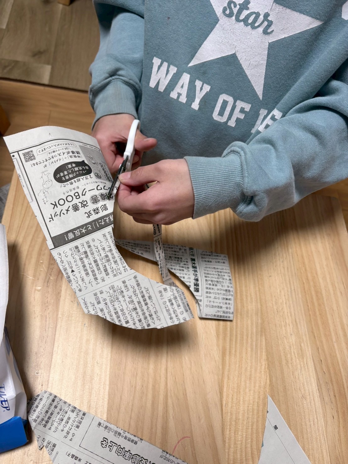 「足元を見つめる、真剣な採寸。」

新聞紙の上に足を置き、「これくらいかな？」とハサミを入れる場所を真剣に考えるお子様の横顔。