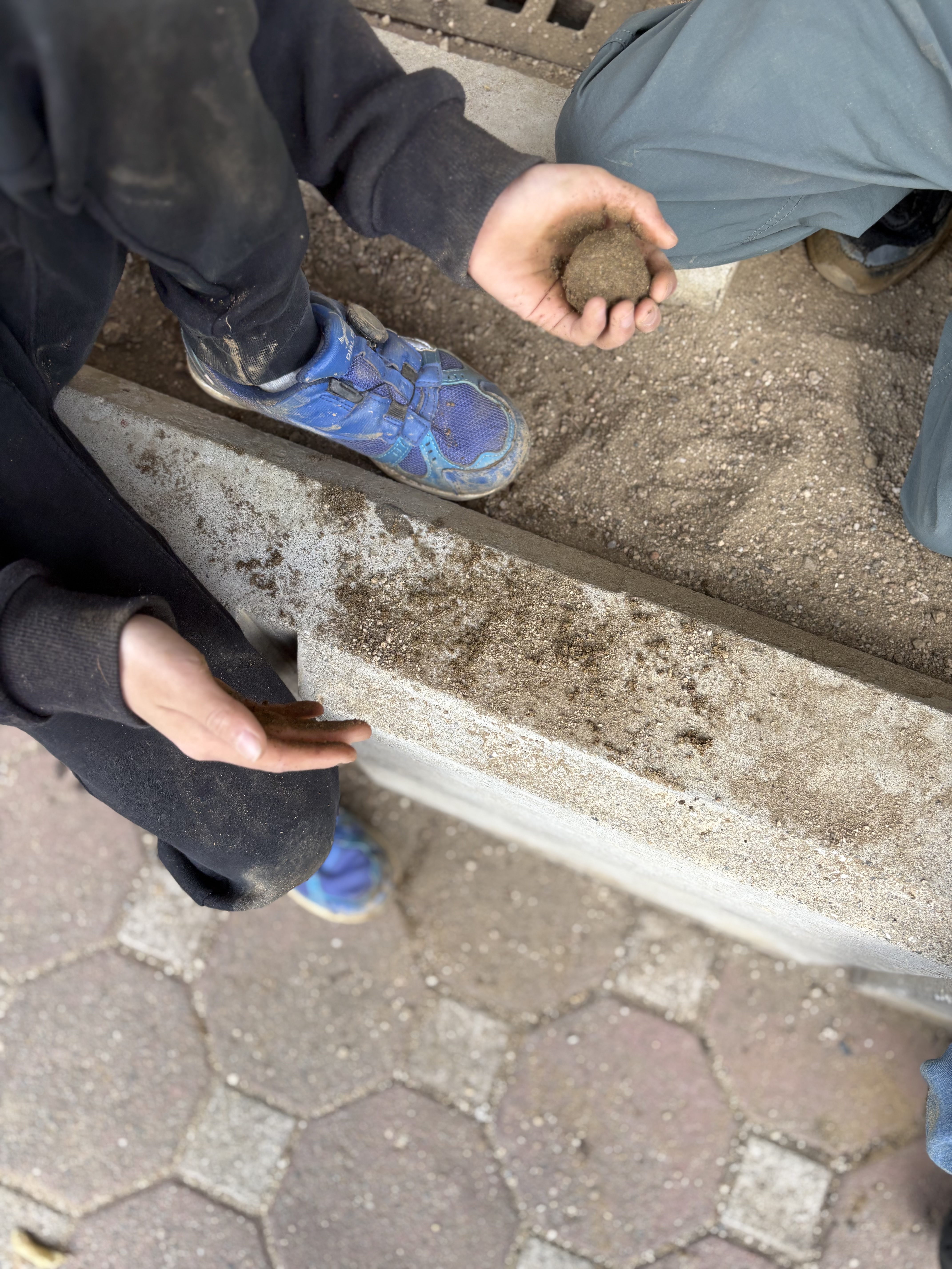 「ギュッギュッの、リズム。」
泥を丸める手の動きを、小学生が身を乗り出して真剣に覗き込む「共同注視」の瞬間。