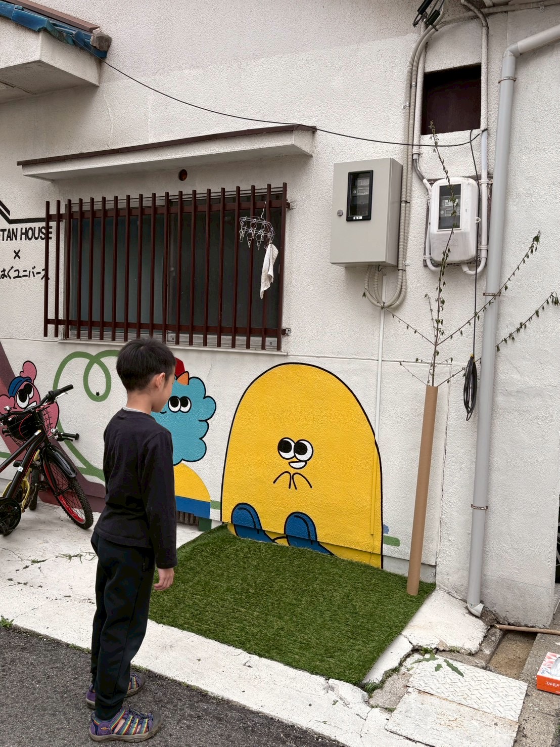 「足裏から伝わる、緑の魔法。」

新しく敷かれた芝生の上で、靴を脱いで感触を確かめるお子様の足元。背景には「ちぐはぐユニバース」さんの鮮やかなアート。