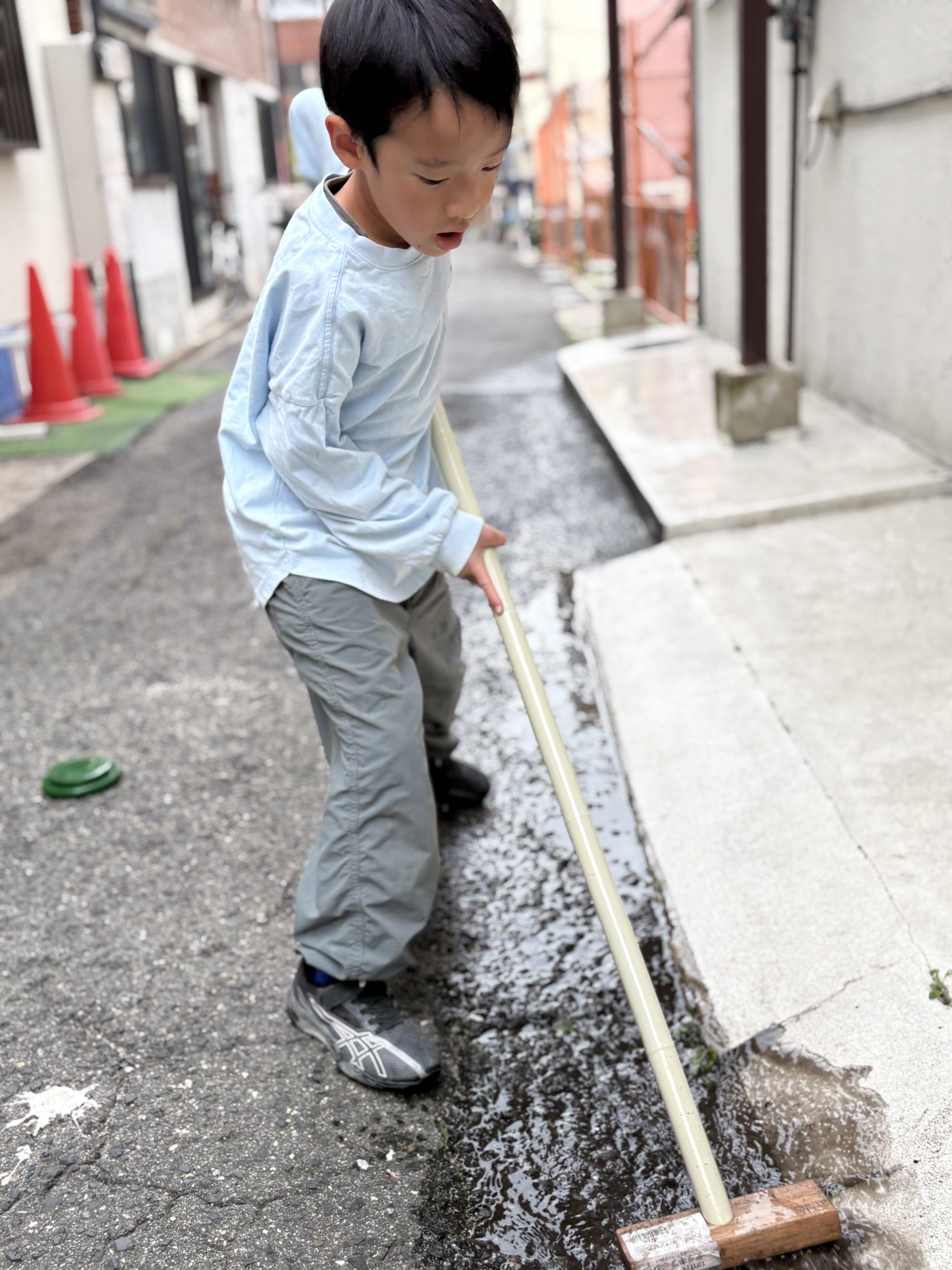 「磨き上げ完了！キラキラの足元。」

掃除を終え、ピカピカになった壁画の前で、ほうきを杖に達成感あふれるピースサイン。
