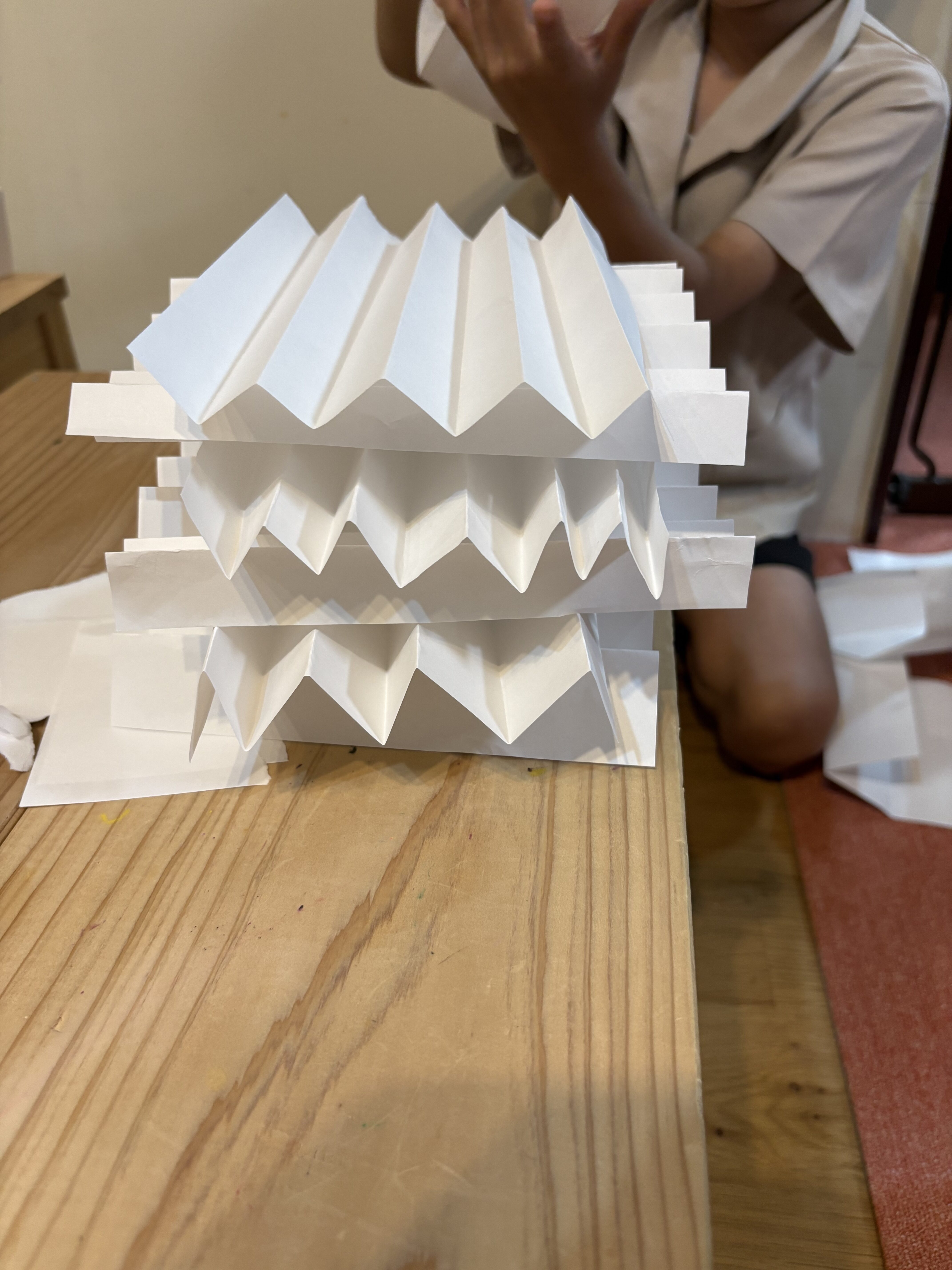 「指先に集中!土台のパーツ作り。」
崩れない土台を作るために、紙の端をきれいに揃えて折る「微細運動」の手元クローズアップ。