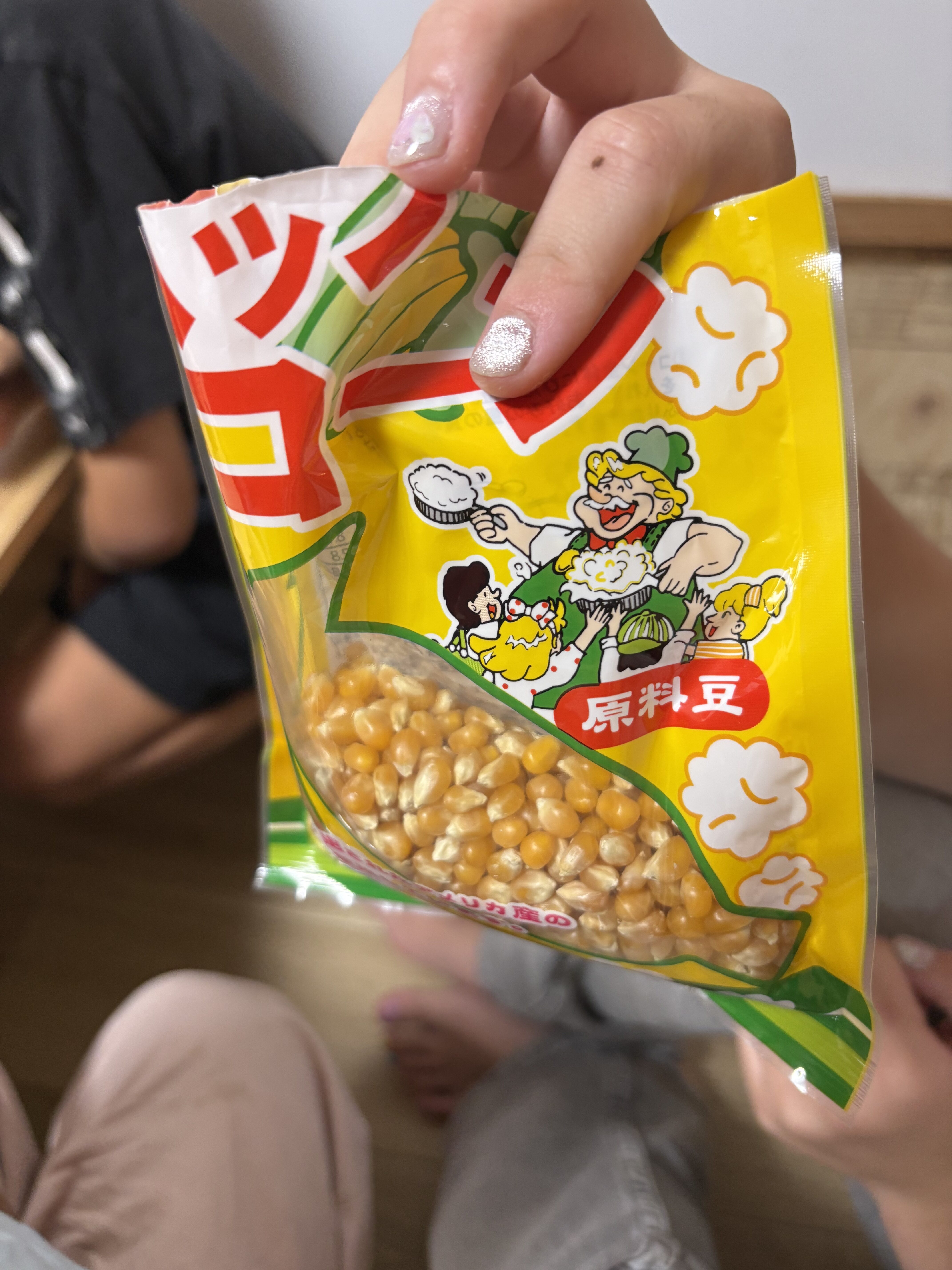 「『この小さな豆がポップコーンになるの？』原料豆に興味津々」
小さくて硬いポップコーンの原料豆を手のひらに乗せ、「不思議〜！」と覗き込む手元のアップ。