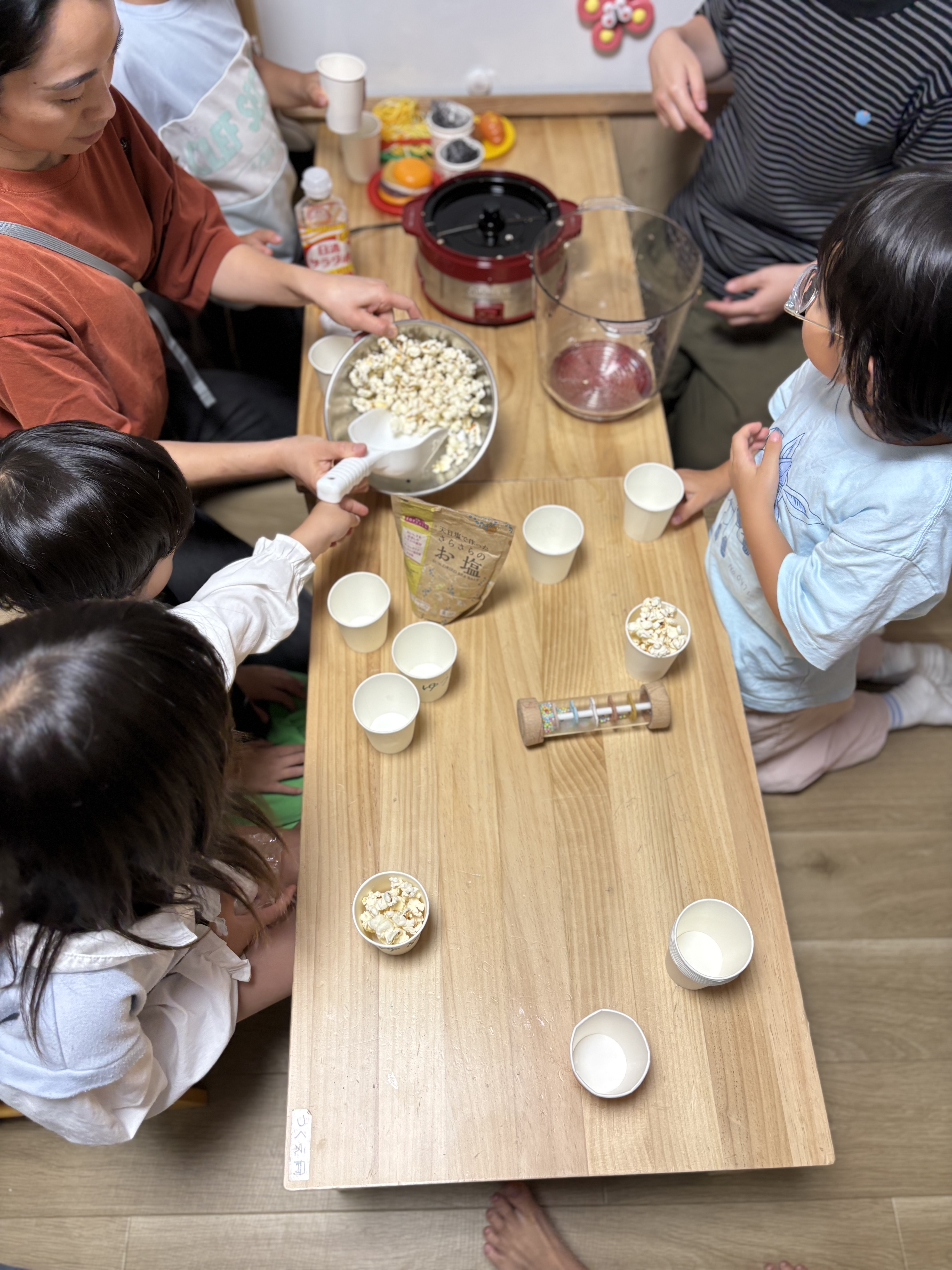 「『自分のカップにたっぷり！』丁寧に取り分けるお楽しみの手元」
大きなボウルから自分の紙コップへ、こぼさないようにそーっとポップコーンを移す真剣な手元。