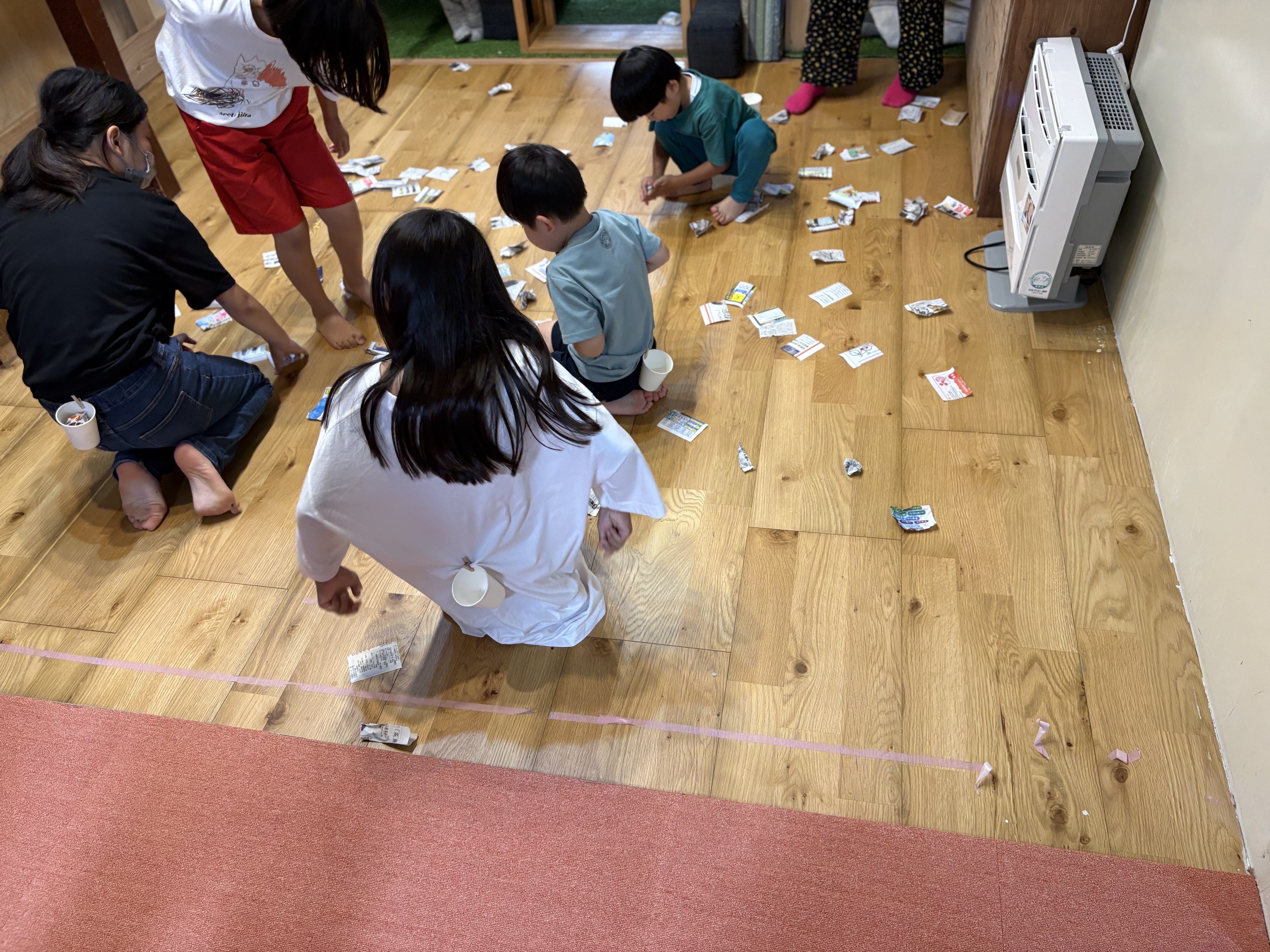 「しゃがんで・立って！全身を使って新聞紙をキャッチ」
深くしゃがみ込んで新聞紙を拾い上げる、足腰の運動が伝わる躍動的なカット。