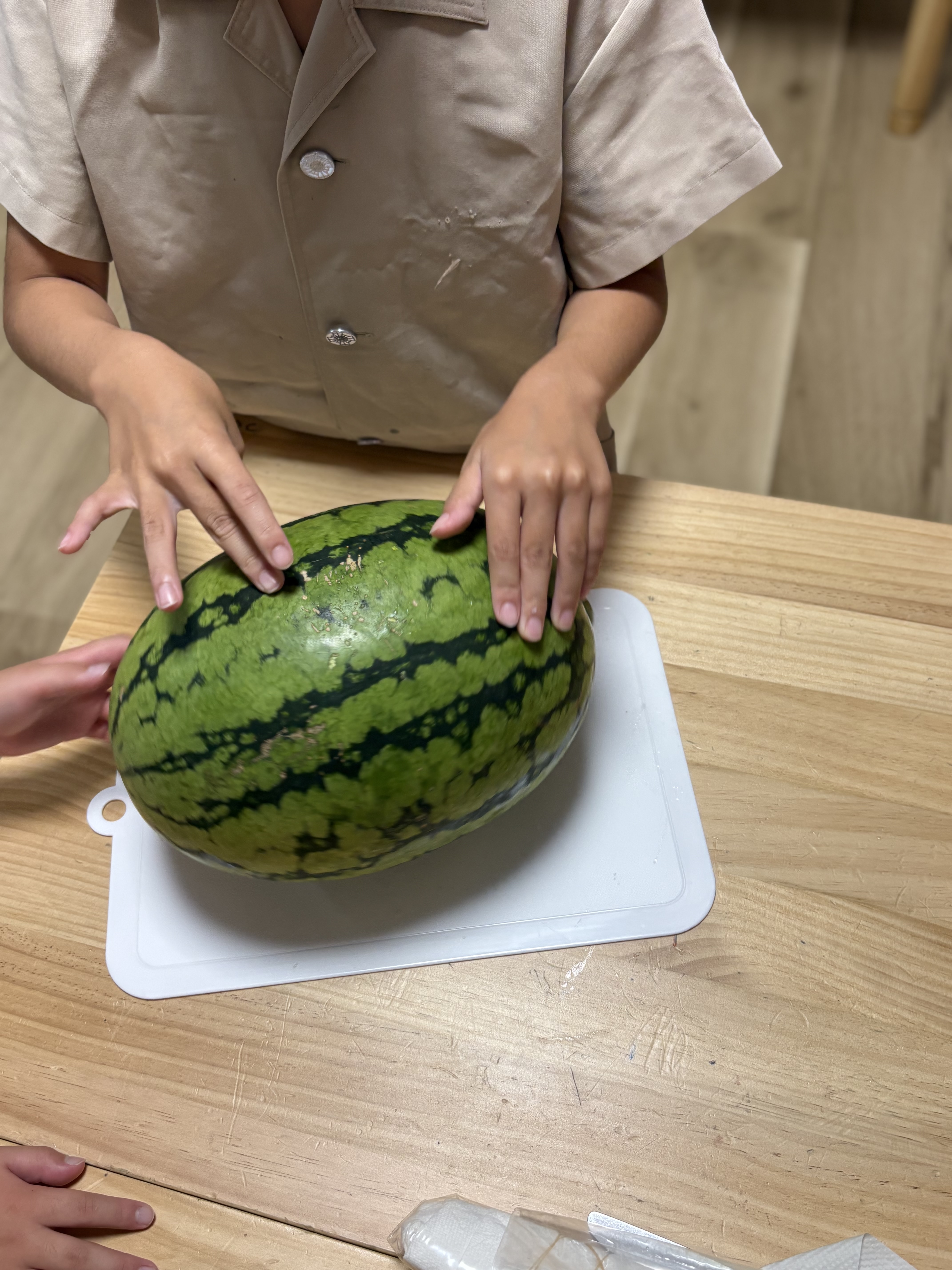 「『トントン！いい音する？』食べる前のワクワク手触りチェック」
スイカをポンポンと叩いたり、撫でたりしながら中身を想像して笑顔を見せる一コマ。