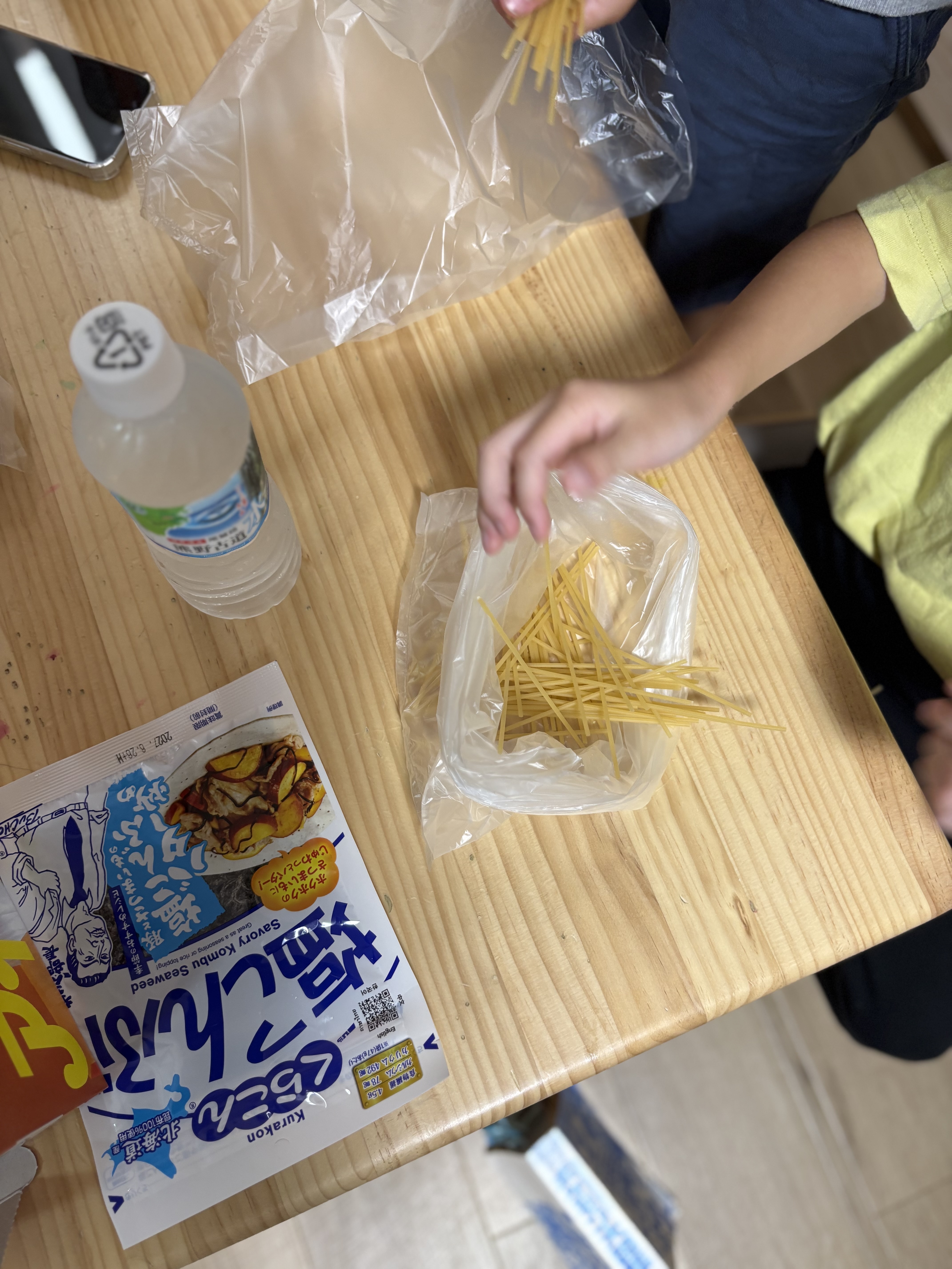 「『お水を注いで…本当にこれで柔らかくなるの?』疑問と不安の表情」
計量カップからお水を注ぎ入れ、「固いよ?」「本当に食べられるの?」と首をかしげる子どもたちの真剣&不思議そうな表情。