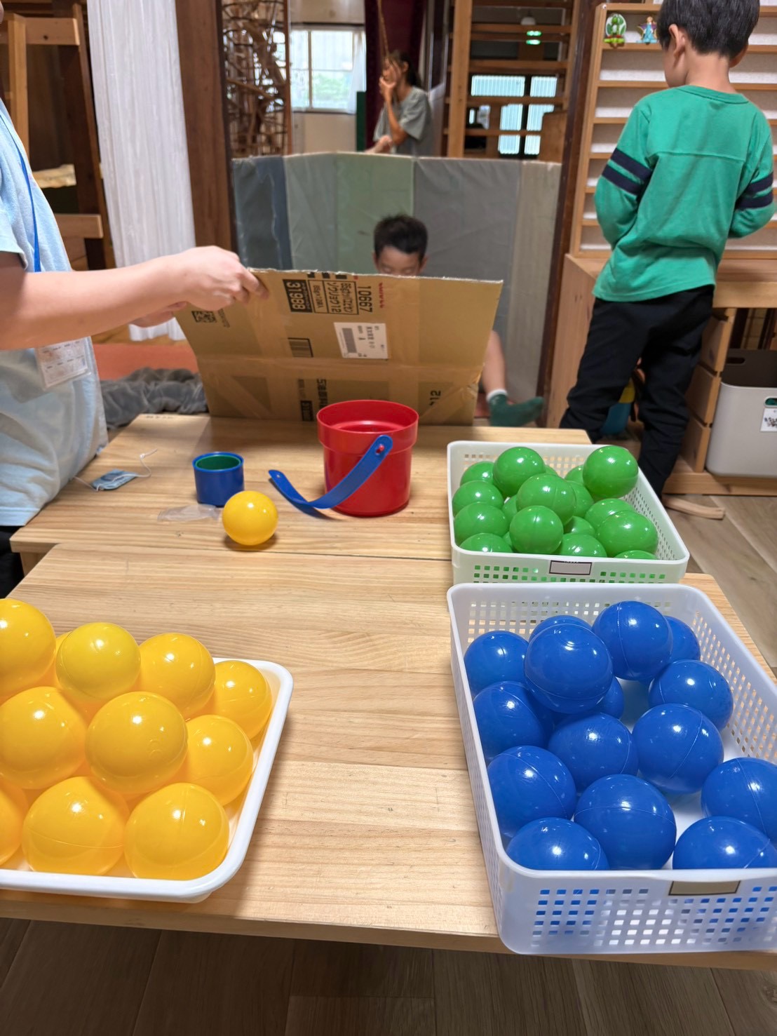 「『坂道の頂上からボールがコロコロ!』ワクワクのスタートカット」
段ボールの坂道のてっぺんでボールを構えるお友達と、両手に黄色と緑のカップを握りしめて身構える挑戦者のオープニングショット。