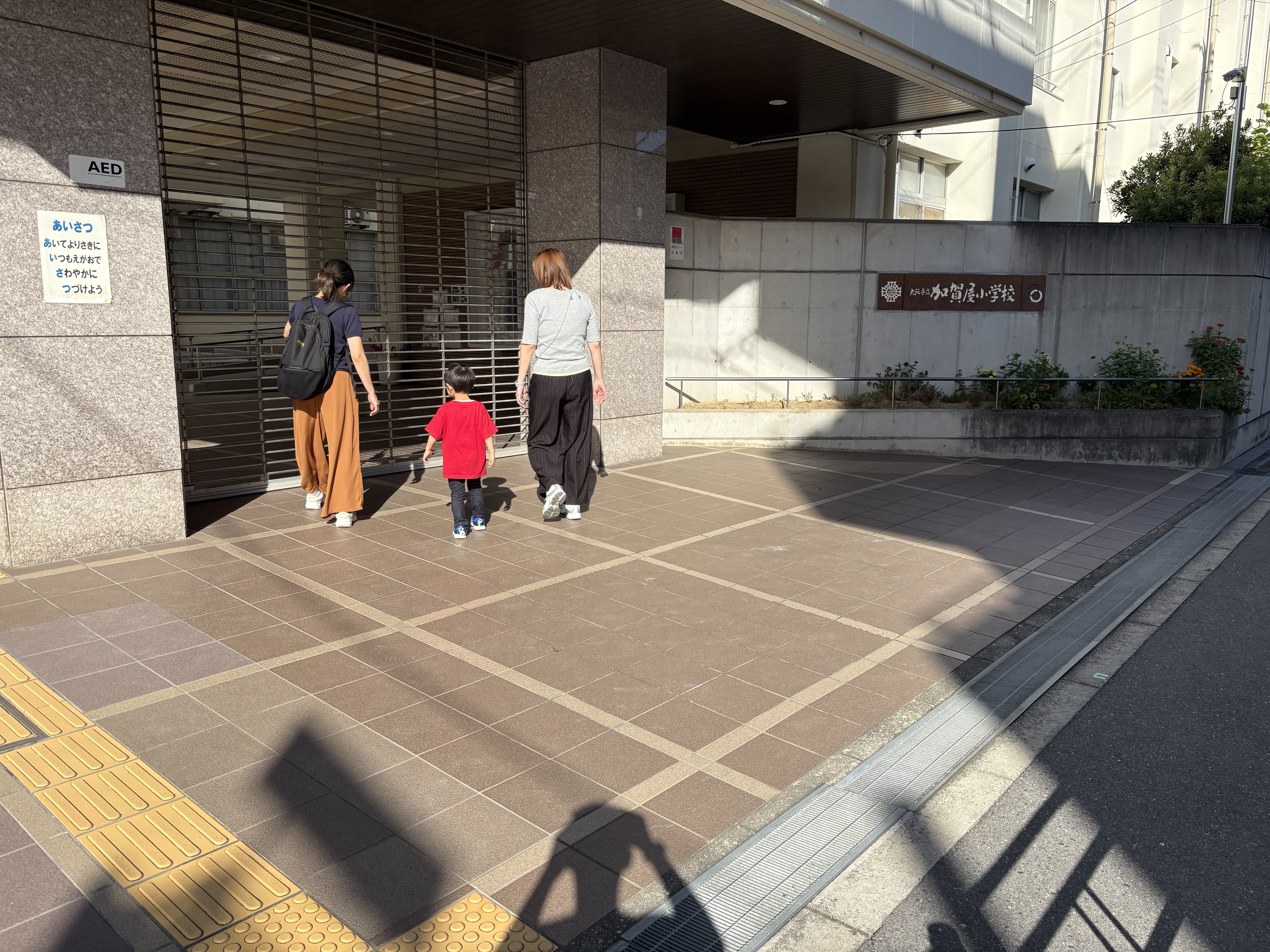 「『無事に指定避難所の小学校に到着！』校門前での確認ショット」
指定避難所である「歩いてすぐの小学校」の校門前に到着し、「ここまで来れば安心だね！」と確認し合う一コマ。