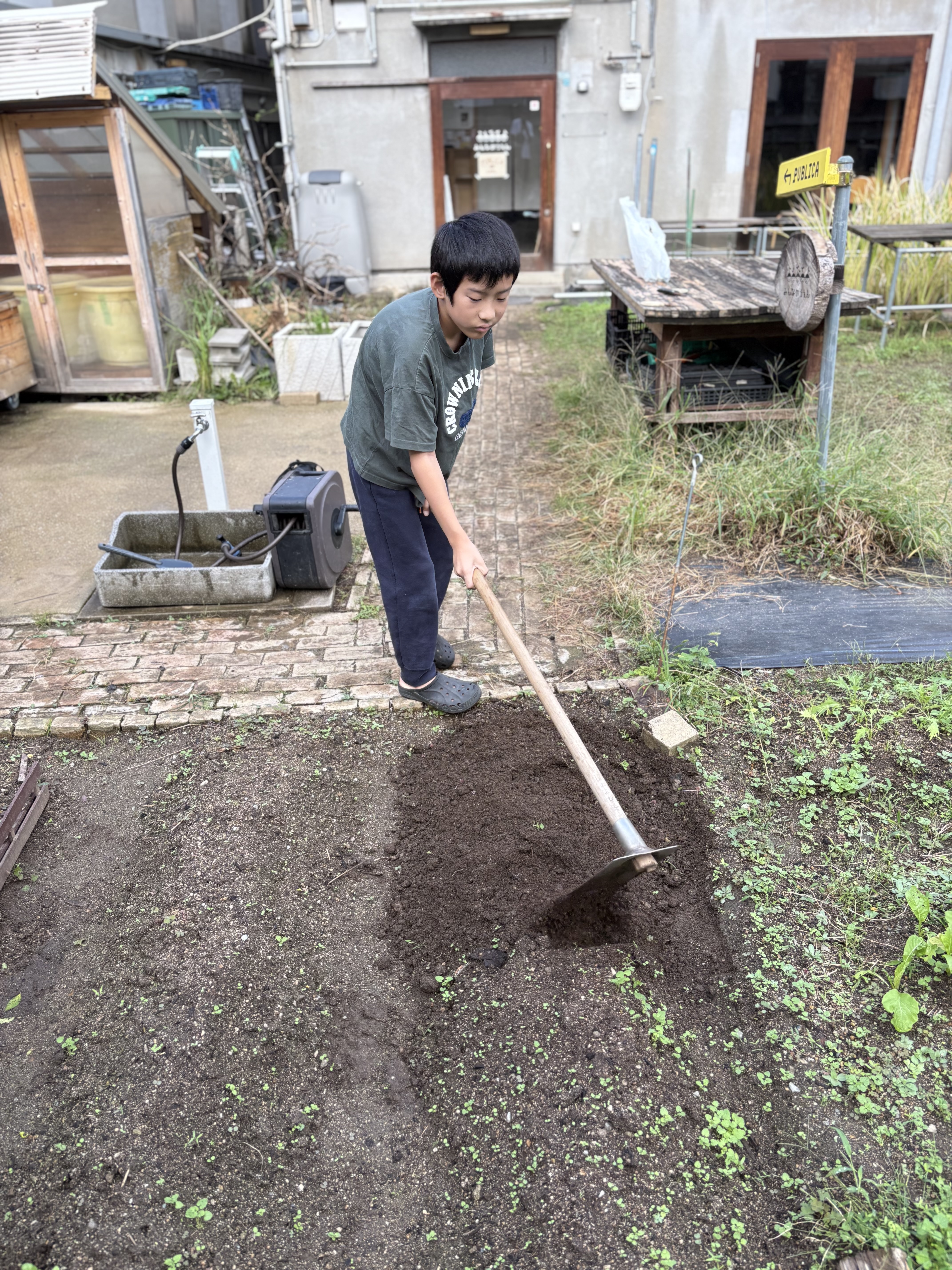 「『こばやん先生、僕も手伝うよ!』小さなクワを手に力強く耕すチャレンジャー」
代表の姿に刺激された子どもが、小さなクワやシャベルを両手で力強く握りしめ、土を耕す頼もしい横顔。