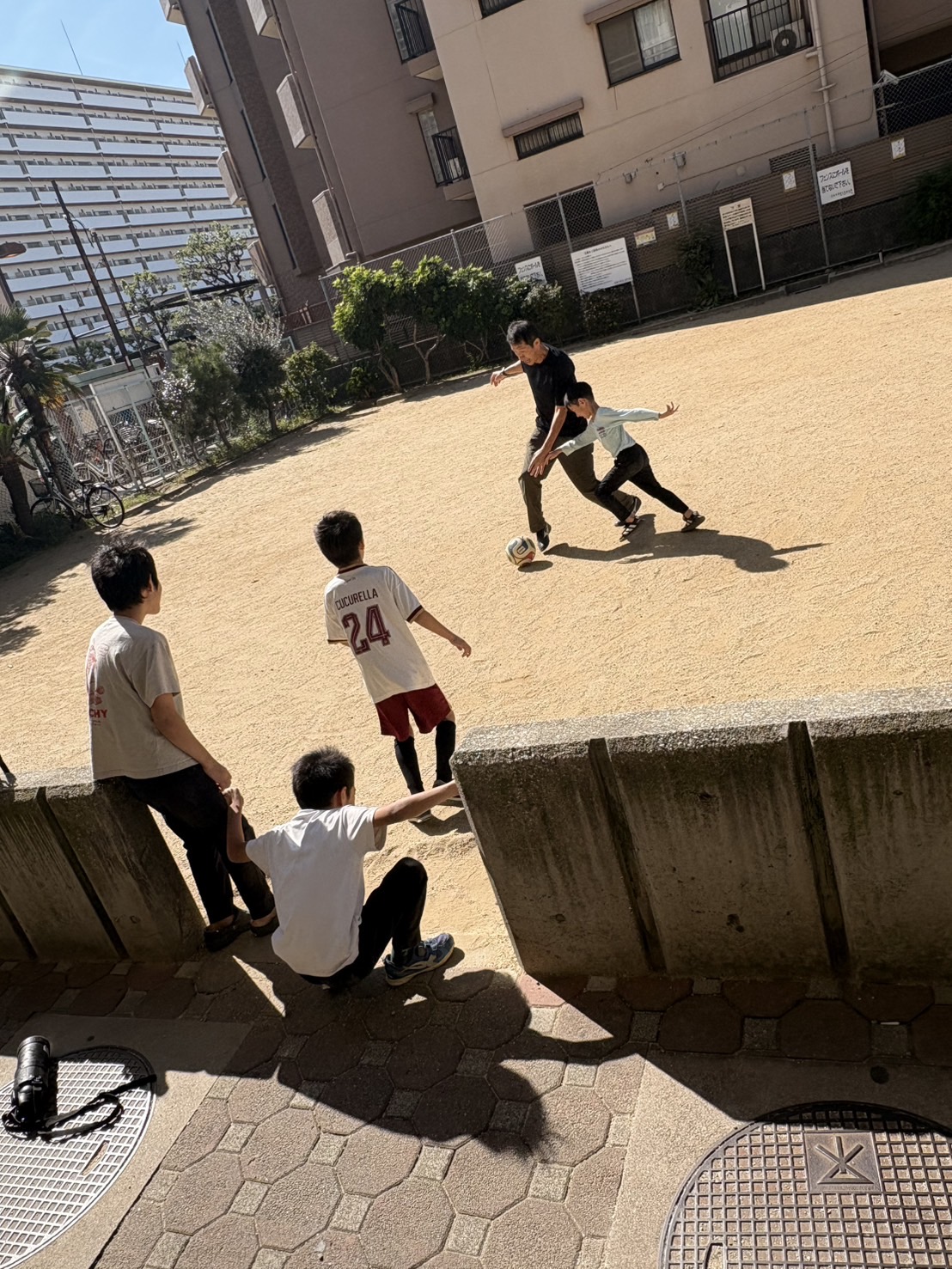 「『こばやん先生にも手加減なし!』本気モードのボール奪い合い」
小林代表がキープするボールに対し、子どもたちが素早いアプローチで足を出して奪いにいく、迫力満点のアクションショット。